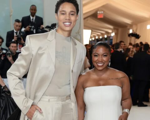 Smiling couple posing on a red carpet with photographers in the background.