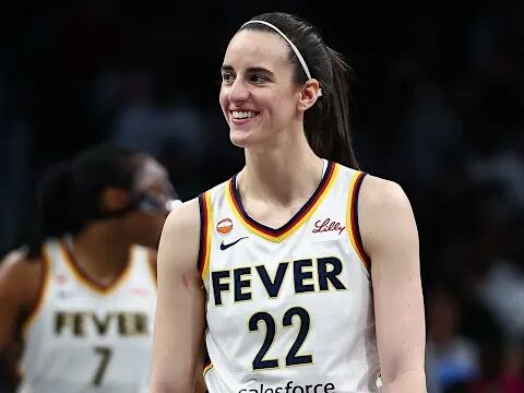Female basketball player in a Fever jersey #22 smiling on the court, with a teammate in the background.