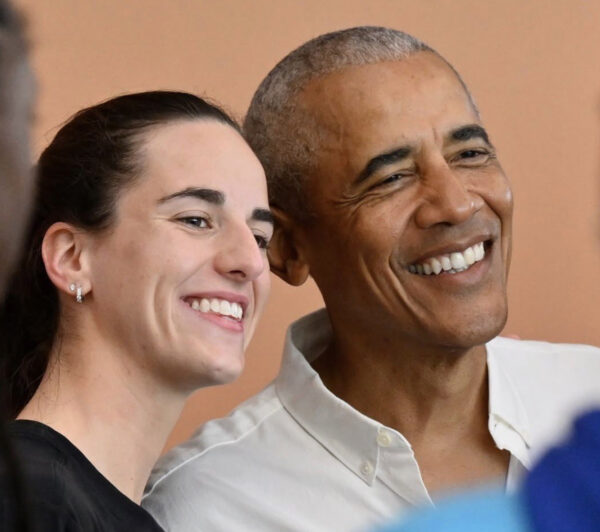 Close-up of two adults smiling warmly, a woman with dark hair and an earring beside a smiling man in a white shirt against a peach background