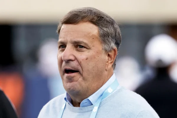 Close-up of a middle-aged man speaking, wearing a light blue sweater and a lanyard at an event