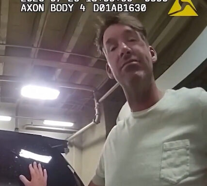 Body-worn camera frame: man in a light green shirt beside a black car in a garage; timestamp and AXON logo visible.