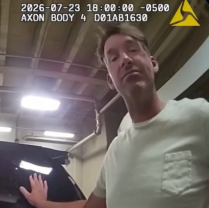 Body-worn camera frame: man in a light green shirt beside a black car in a garage; timestamp and AXON logo visible.