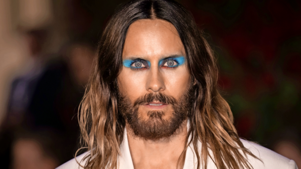 Close-up portrait of a person with long hair and bold blue eyeshadow, wearing a white jacket.
