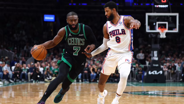 Two NBA players in a heated moment on the court, Celtics in green and 76ers in white chasing the ball amid a crowded arena.