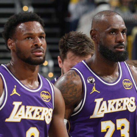 Two Los Angeles Lakers players in purple jerseys stand on the basketball court during a game, focused expressions, blurred crowd in the background.