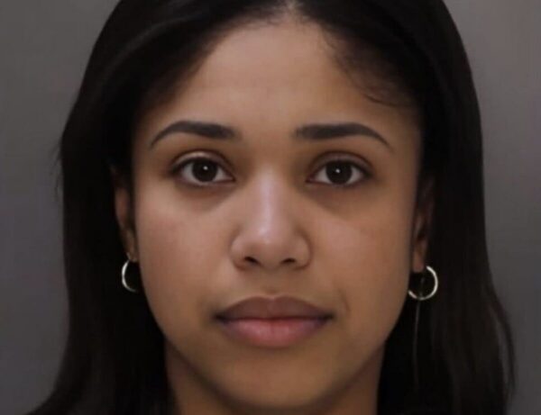 Mugshot of a young woman with dark hair and hoop earrings, looking straight ahead against a gray background.