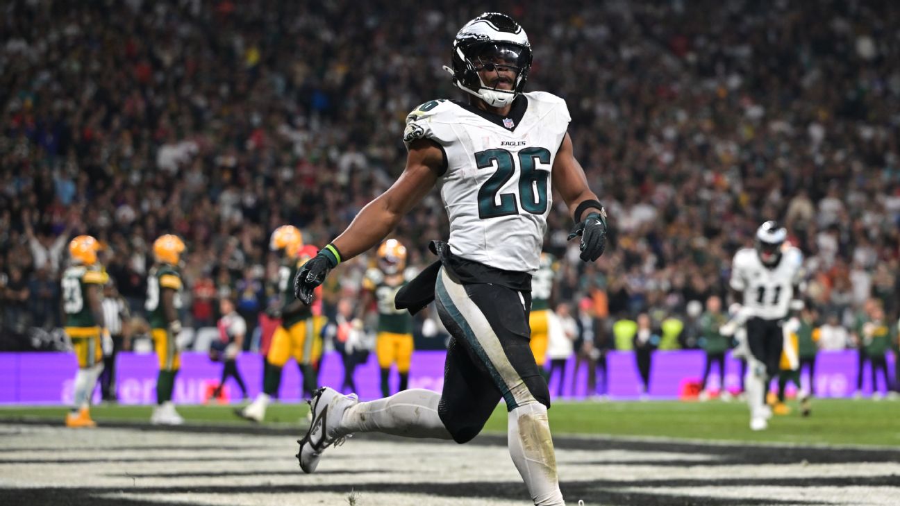 Philadelphia Eagles player number 26 running on the field during a game with a packed crowd in the stands behind him.