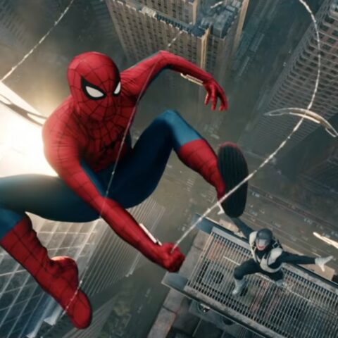 Spider-Man swings between skyscrapers above a city, feet extended, chasing a figure on a high ledge below him.
