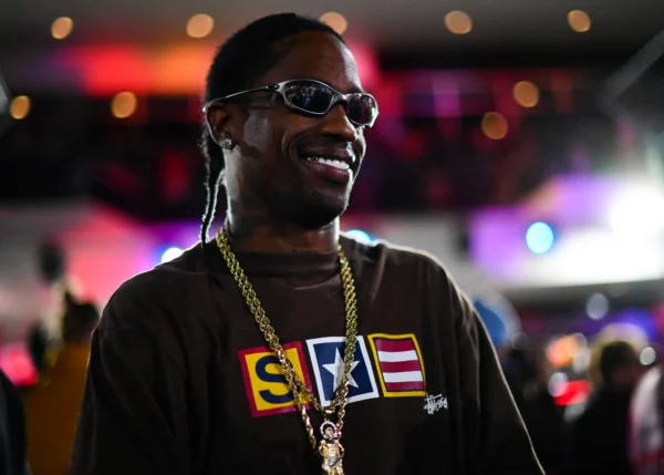 Smiling man wearing sunglasses and thick gold chains at a colorful nightlife venue (close-up shot)