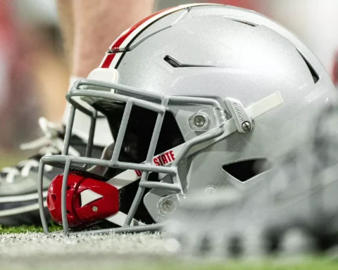 Football helmet lying on artificial turf with a red mouthguard and cleats in the background.