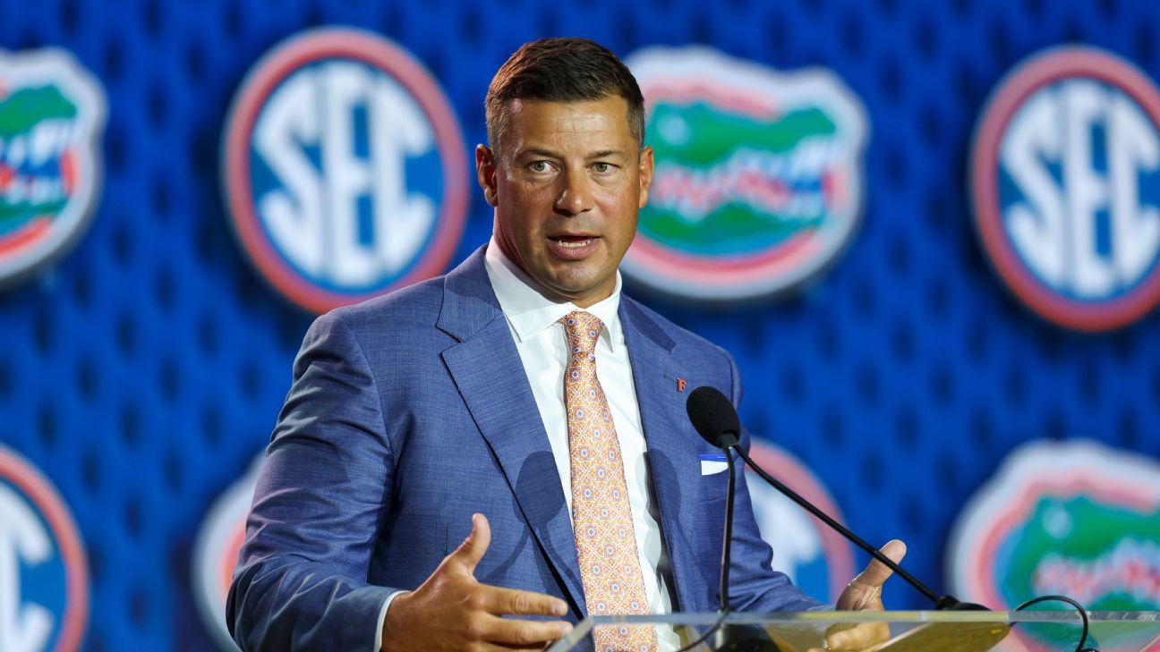 Man in a blue suit speaking at a podium during a press conference, with SEC and Florida logos in the background