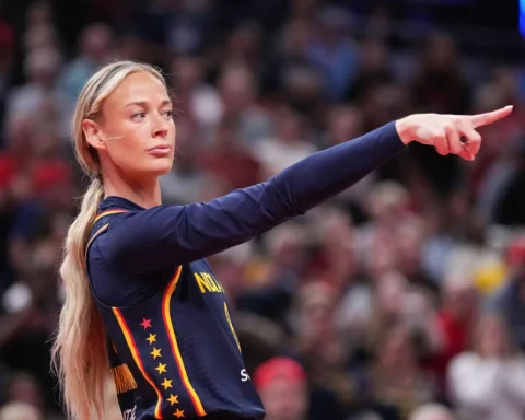 Female athlete in a navy Netherlands uniform with red-yellow trim points to the right during a game, crowd blurred in the background.