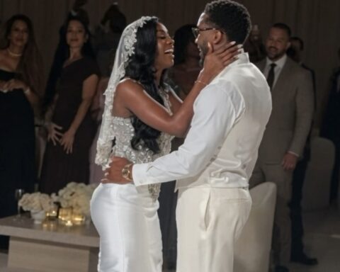 Bride and groom share a joyful kiss-and-dance at their wedding reception, surrounded by guests in evening attire.