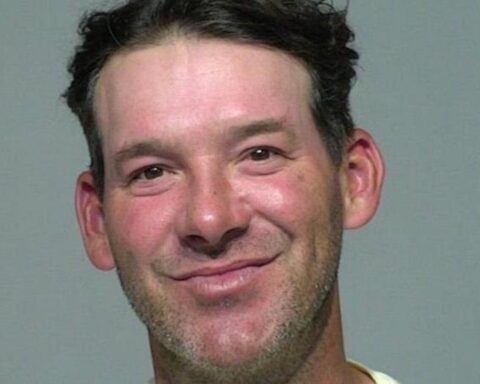 Close-up of a smiling man with short dark hair and light stubble, against a gray background.