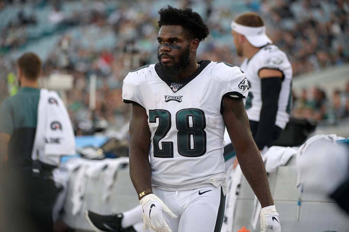 American football player in a white Philadelphia Eagles jersey with number 28 standing on the sideline during a game, focused and ready to return maneuvers upfield.