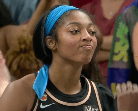 Young woman in a blue headband and black athletic jersey at a crowded event, looking to the side.