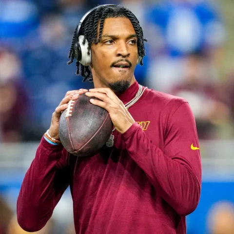 Athlete in a burgundy long-sleeve shirt wearing headphones, gripping a football and looking ready to throw.