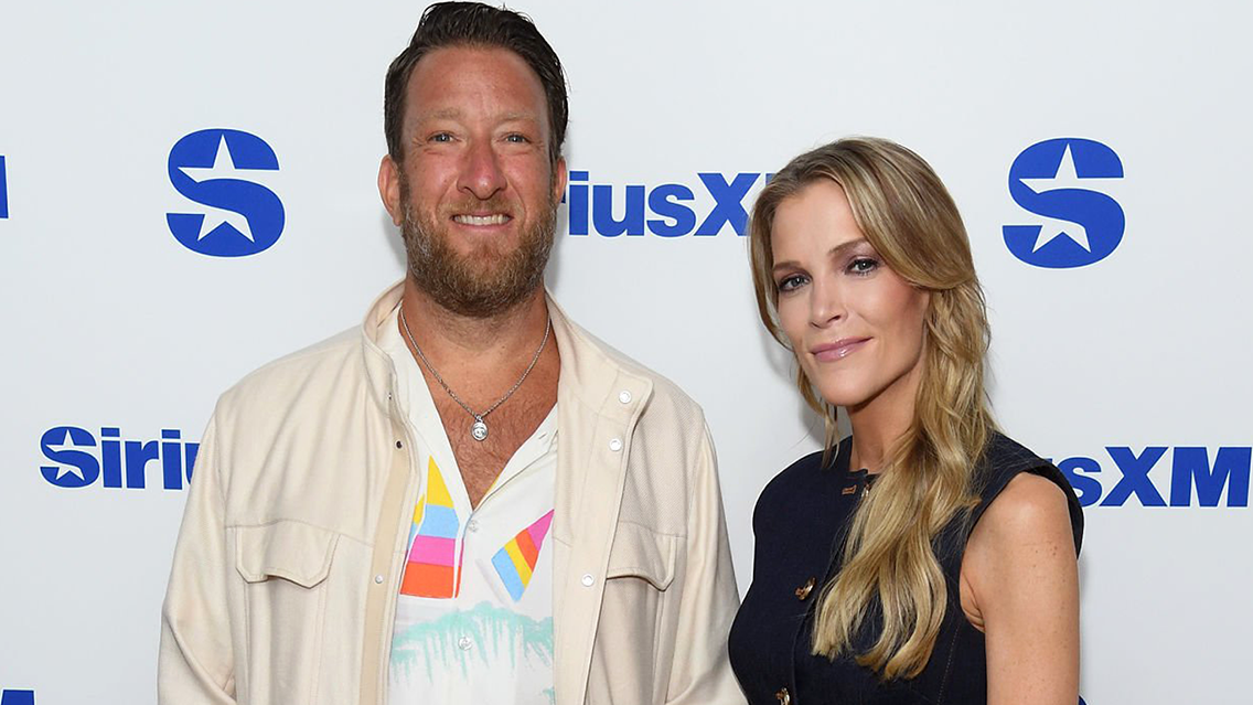 Two adults posing for a photo on a SiriusXM backdrop; man in a light jacket and tropical shirt, woman in a dark sleeveless dress.