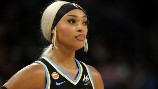 Close-up of a female basketball player with platinum blonde hair, black headband, wearing a blue-and-black jersey.