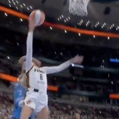 Basketball player in a white jersey (#8) dunks the ball over a blue-clad defender in a crowded arena.