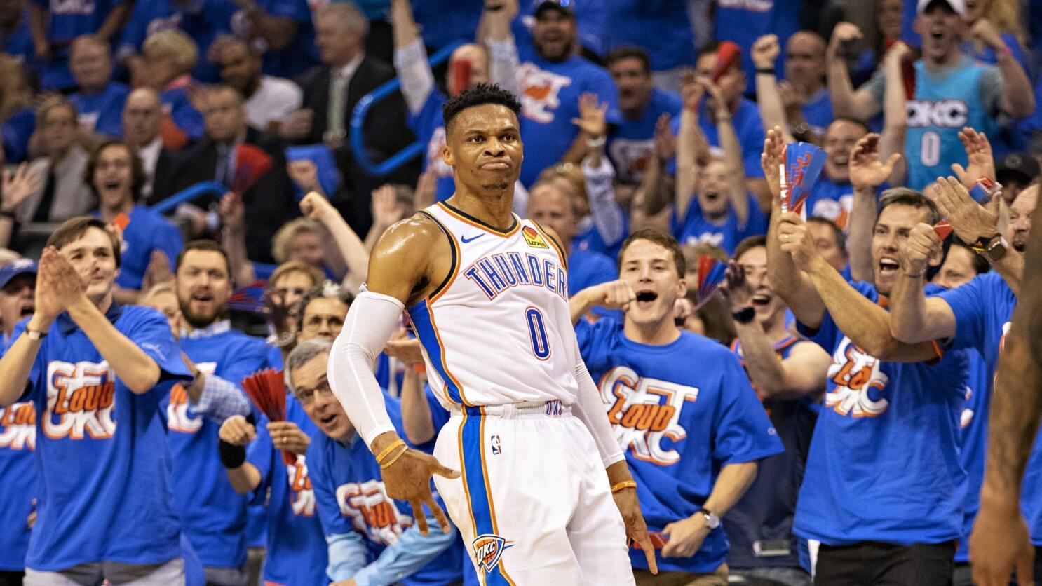 Thunder basketball player wearing number 0 walks past a cheering crowd in blue shirts at a game, fans raising arms in celebration behind him
