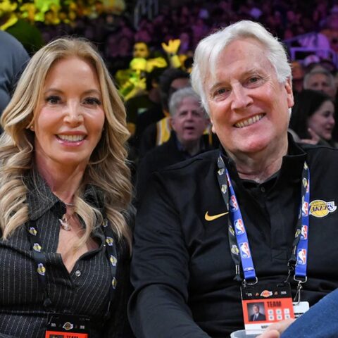 Two smiling adults sit courtside at a basketball game, wearing Lakers lanyards and credentials.