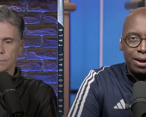 Two men host a podcast in a studio, each with a microphone, split by a vertical divider with brick wall on the left and blue set on the right.