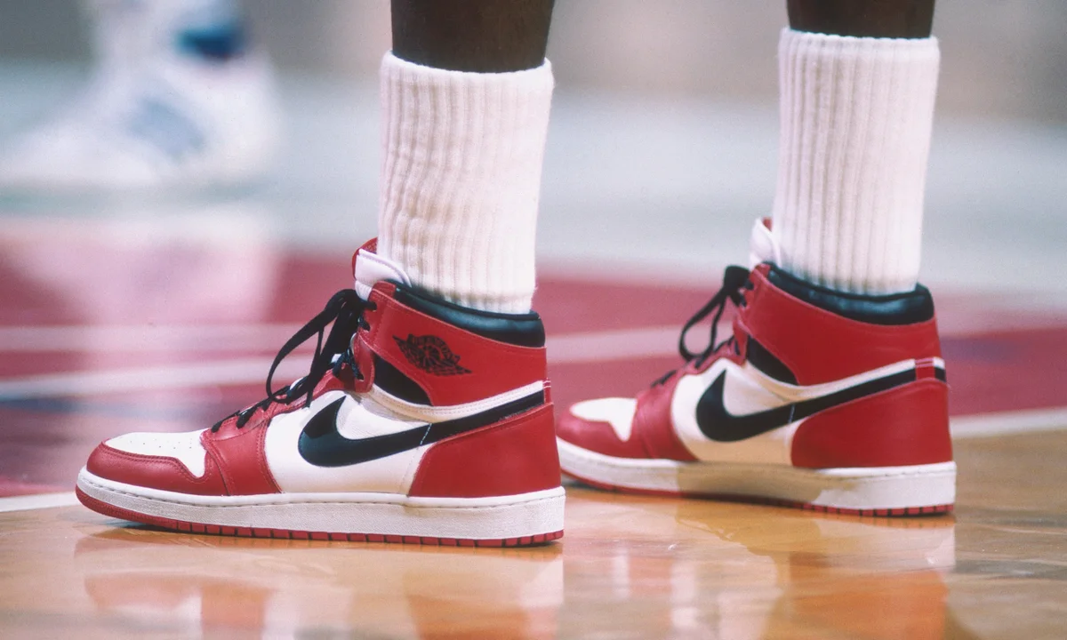 Person wearing red, white, and black Air Jordan 1 sneakers on a basketball court with white socks visible above the shoes