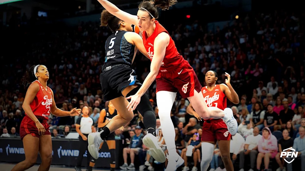 Women’s college basketball players leap for the ball during a fast-paced game, red Indiana uniforms against a black-clad opponent, crowded arena in the background.